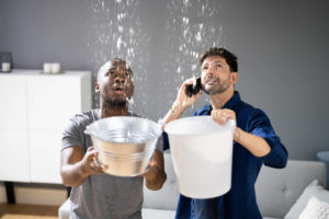 Two men holding buckets that water leak is dripping into
