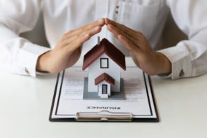 Person's hands over model of house and insurance papers